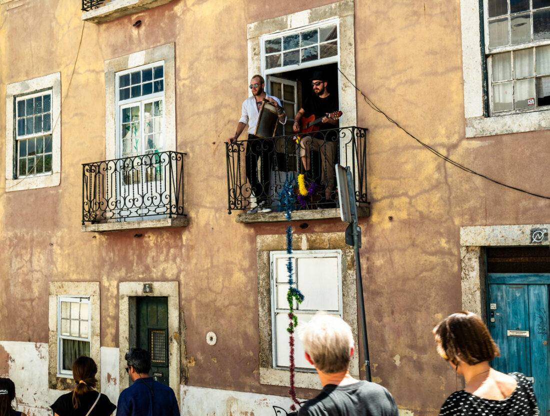 zwei junge Männer stehen auf einem Balkon eines alten Hauses in Porto und machen ihre House-Musik, einer mit der Gitarre , der andere mit einem alten Waschbrett. Die Fußgänger blicke hinauf und hören zu.