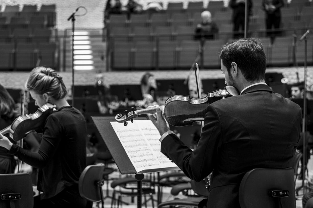 Ein Geigenspieler des Philharmonischen Orchesters der Elphi stimmt vorab sein Instrument ein und wird dabei über die Schulter Mit Blick auf das Notenblatt in Schwarz-Weiß fotografiert