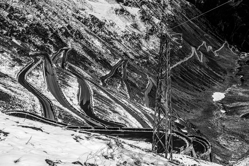 eine Serpentine vom Berggipfel aus fotografiert, die mit zunehmender Höhe durch die Schneegrenze führt.